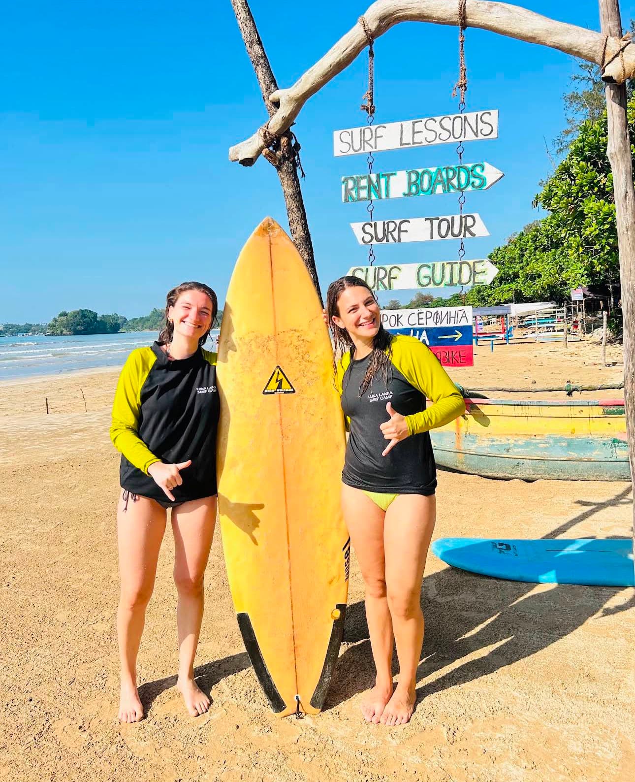 Luna Lanka surfers holding a surfboard near a surf lessons sign