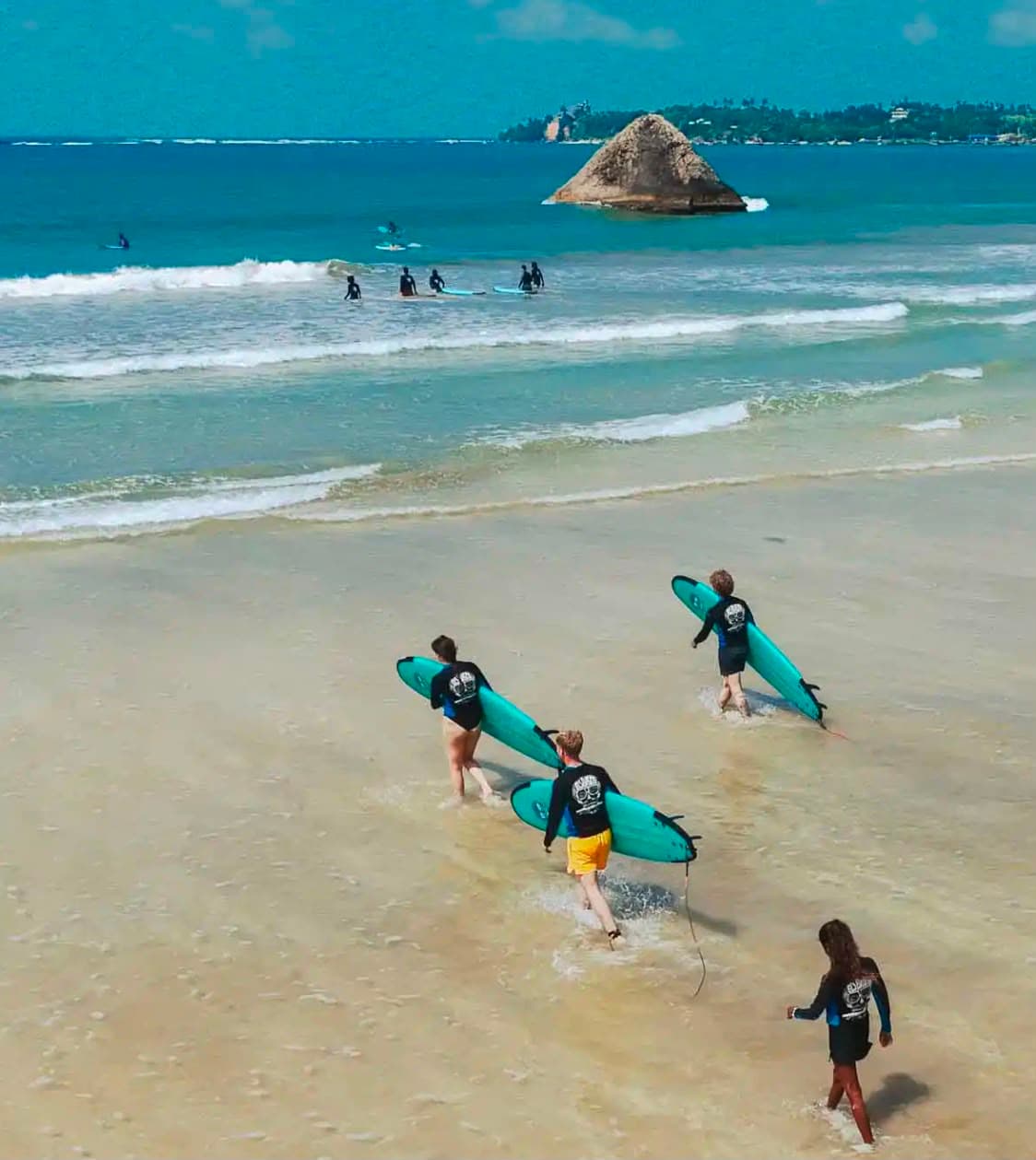 Surfers carrying boards into the water at Weligama